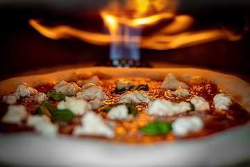 Pizza bäckt in einem Pizzaofen mit Feuer im Hintergrund